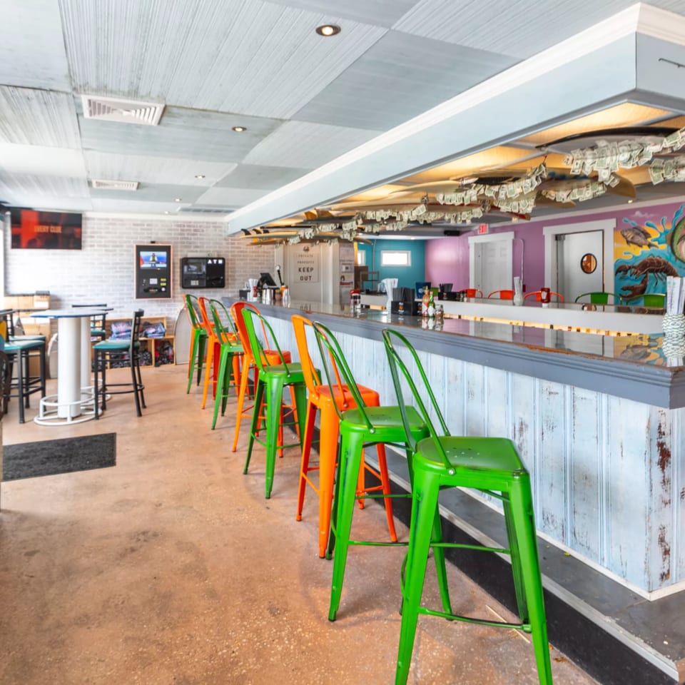 Interior of Island Beach Fish Company bar with colorful stools and money hanging from the ceiling.
