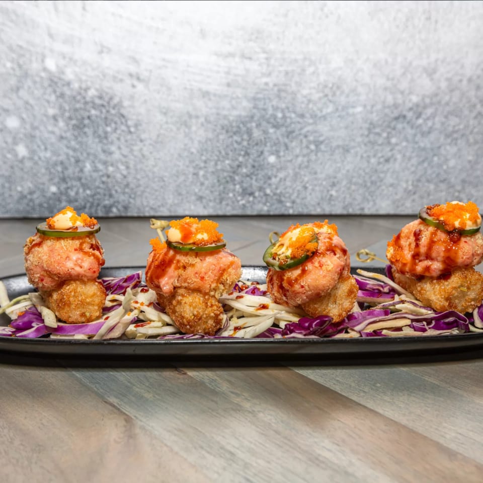 Four Island Beach Fish Company seafood appetizers with sauce, roe, and jalapenos on a bed of cabbage.