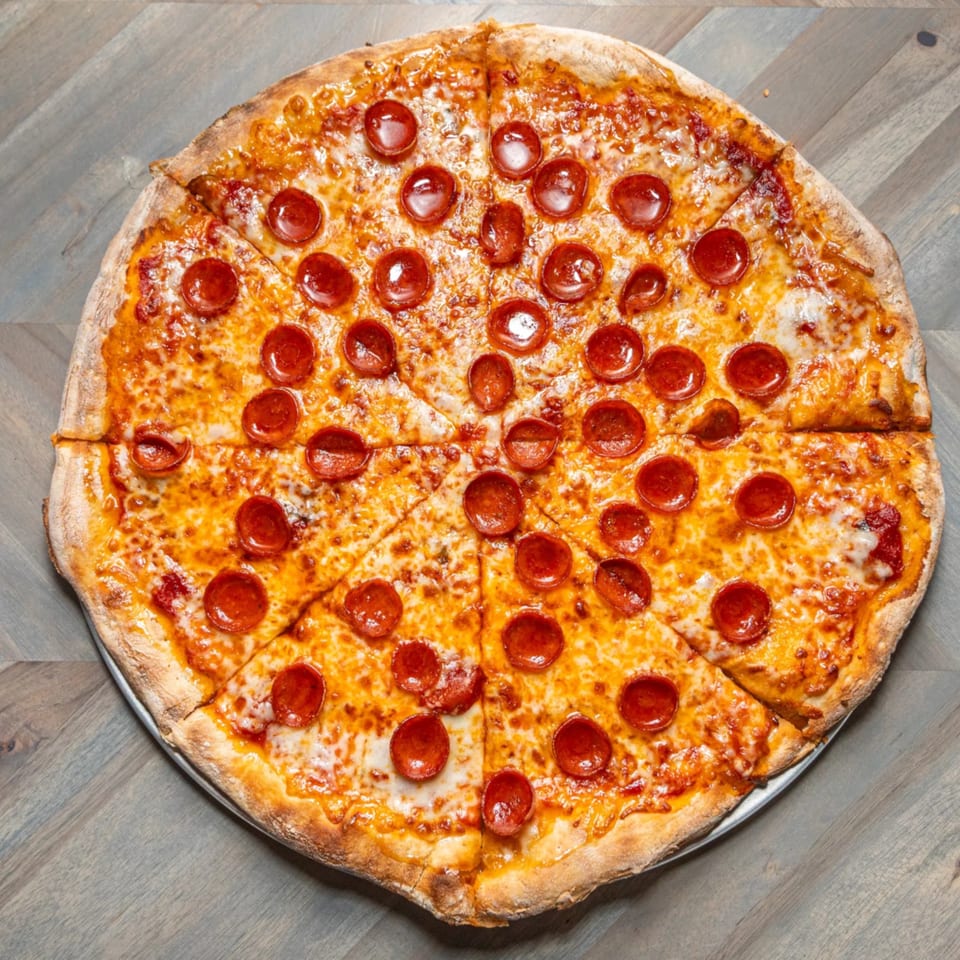 A large, round pepperoni pizza with melted cheese, sliced into wedges on a metal tray.